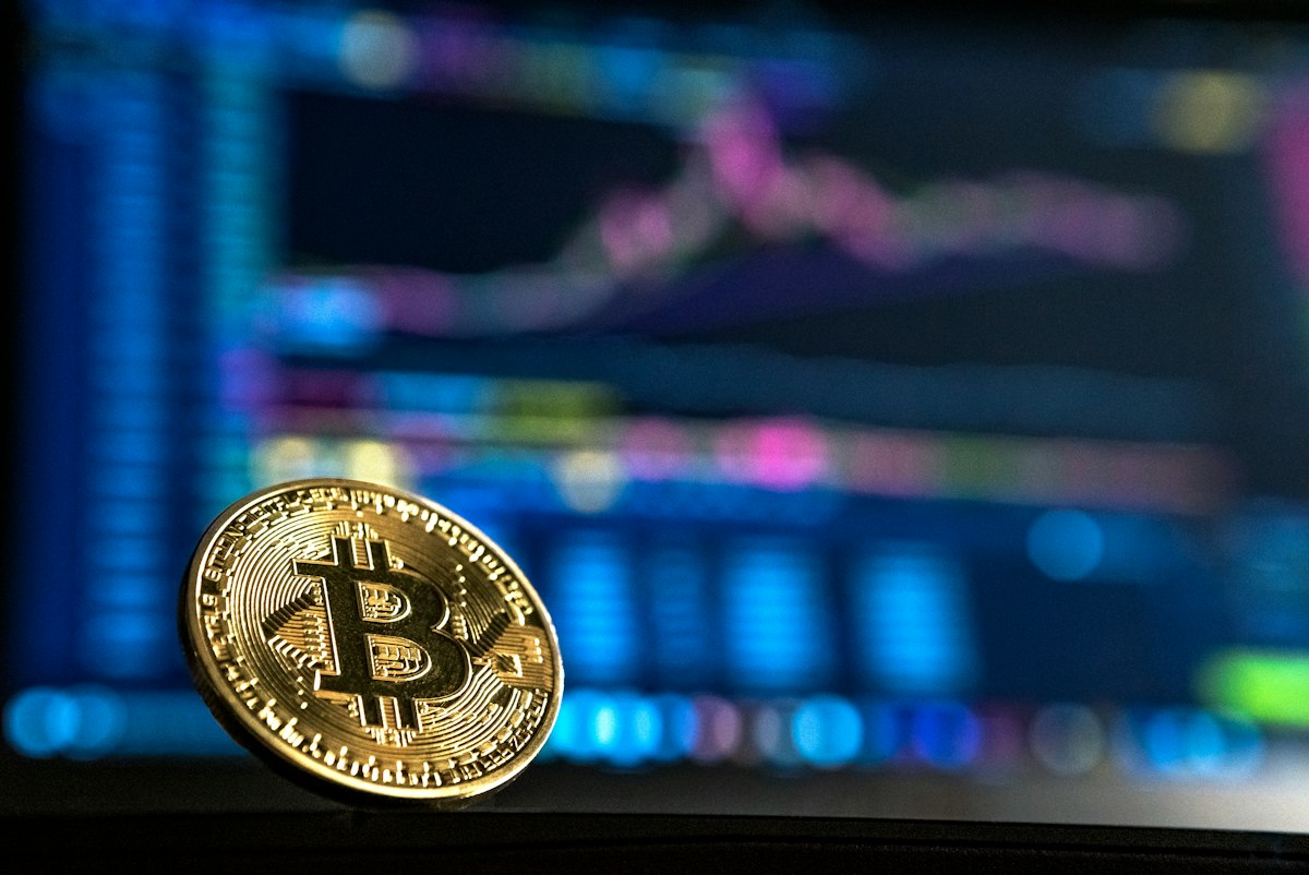 A Bitcoin coin in front of a blurred trading screen